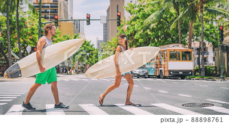 Surfers going surfing in Waikiki beach, Honolulu, Hawaii. USA summer travel vacation happy couple friends walking crossing city street carrying surfboards. Asian woman, Caucasian young man 88898761