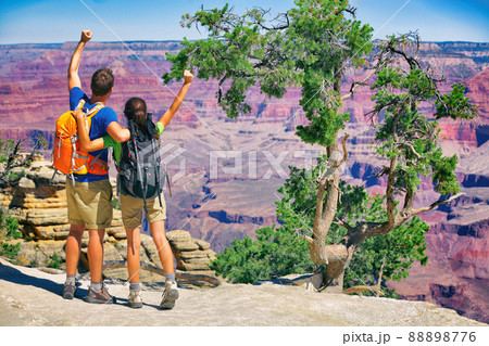 Grand Canyon hikers tourists couple cheering success with arms up happy for hike achievement. Backpackers hiking with backpacks standing at view of famous american landmark, USA trip travel. 88898776