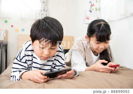 ベッドでスマホを見ているアジア人の子供 88899092