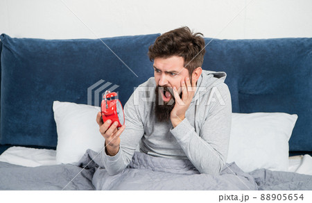 Awaken man shouting in panic looking at alarm clock in bed in morning, oversleeping Awaken man shouting in panic looking at alarm clock in bed in morning, oversleeping 88905654