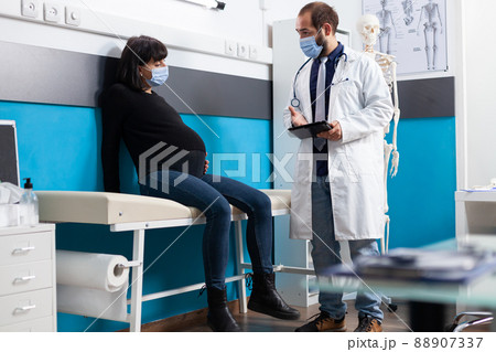 Pregnant adult talking about childbirth with health physician during covid 19 pandemic. General practitioner doing consultation with woman expecting child at checkup visit in medical cabinet. Pregnant adult talking about childbirth with health physician during covid 19 pandemic. General practitioner doing consultation with woman expecting child at checkup visit in medical cabinet. 88907337