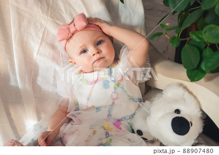serious little girl in beautiful dress sits on an armchair and looks at camera 88907480