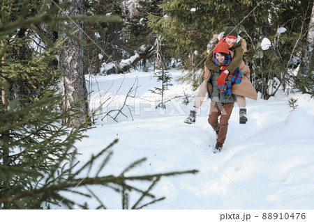 Young Caucasian guy giving his girlfriend piggyback ride while walking in local forest on winter day Young Caucasian guy giving his girlfriend piggyback ride while walking in local forest on winter day 88910476