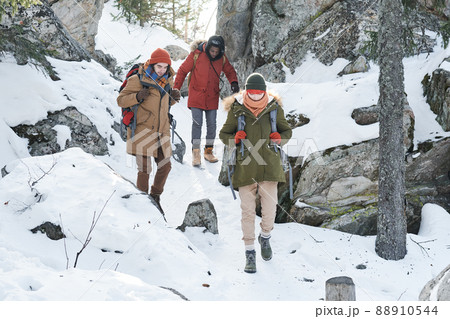 Group of three active young people wearing backpacks walking down the mountain on winter day Group of three active young people wearing backpacks walking down the mountain on winter day 88910544