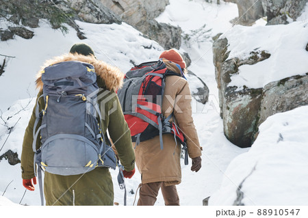 Rear view of unrecognizable young people wearing warm clothes and backpacks hiking in mountains on winter day 88910547