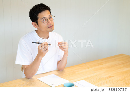 筆ペンを片手にどんな文面にしようか考えている男性 88910737