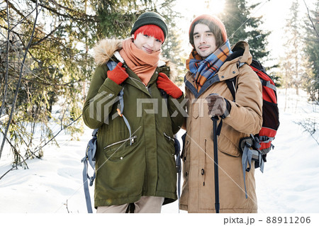 Horizontal medium portrait of active young Caucasian man and woman wearing backpacks posing on camera while hiking on winter day Horizontal medium portrait of active young Caucasian man and woman wearing backpacks posing on camera while hiking on winter day 88911206