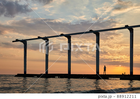 Sea pier at sunset, where a girl is sunbathing and fishermen are fishing 88912211