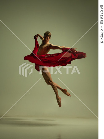 One young muscled man, flexible ballet dancer in action with red fabric, cloth isolated on olive color background. Theater, emotions, grace, art, beauty concept. 88912598