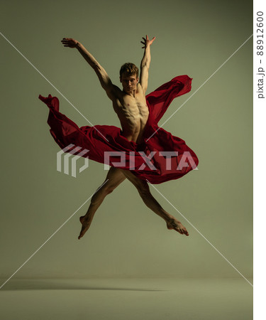 Flight. One young muscled man, flexible ballet dancer in action with red fabric, cloth isolated on olive color background. Theater, emotions, grace, art, beauty concept. 88912600