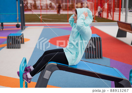 Caucasian woman in mint sweatshirt doing abdominal exercises outdoors. Caucasian woman in mint sweatshirt doing abdominal exercises outdoors. 88913267