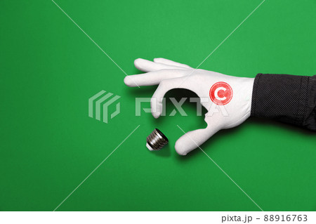 International Intellectual Property Day. A hand in a white glove with a copyright sign, depicts a light bulb, with the outline of a human face. Green background. The concept of copyright and ideas International Intellectual Property Day. A hand in a white glove with a copyright sign, depicts a light bulb, with the outline of a human face. Green background. The concept of copyright and ideas 88916763