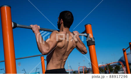 Shirtless man pulling up on horizontal bar outdoors. Shirtless man pulling up on horizontal bar outdoors. 88917296