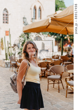 Girl Tourist Walking Through Ancient Narrow Street On A Beautiful Summer Day In MEDITERRANEAN MEDIEVAL CITY, OLD TOWN BUDVA, MONTENEGRO. Young Beautiful Cheerful Woman Walking On Old Street At Girl Tourist Walking Through Ancient Narrow Street On A Beautiful Summer Day In MEDITERRANEAN MEDIEVAL CITY, OLD TOWN BUDVA, MONTENEGRO. Young Beautiful Cheerful Woman Walking On Old Street At 88917498