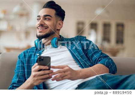Young man in a blue tshirt with a phone in hands sitting on the sofa Young man in a blue tshirt with a phone in hands sitting on the sofa 88919450