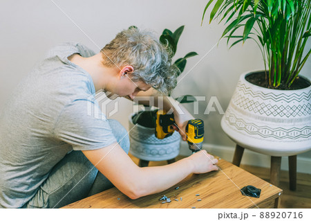 A young man with an electrical screwdriver assembles a tv stand console according to instructions in his new house. Man assembling furniture at home using a cordless screwdriver. Selective focus. 88920716