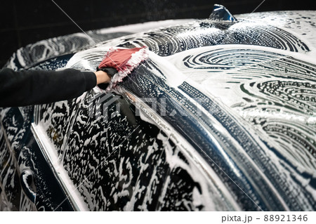 Professional car wash. Detailing worker washes the vehicle body with foam and rag Professional car wash. Detailing worker washes the vehicle body with foam and rag 88921346