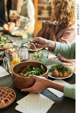 Close-up of boy putting fresh vegetable salad from bowl on his plate during dinner at table with his family Close-up of boy putting fresh vegetable salad from bowl on his plate during dinner at table with his family 88922537