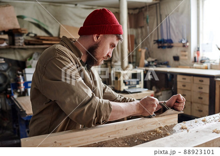 Modern young bearded Caucasian woodworker using hand plane to smooth and shape wooden plank 88923101
