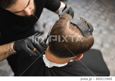 Hairdresser scissors hair on the head sides for a stylish black-haired man in the barbershop Hairdresser scissors hair on the head sides for a stylish black-haired man in the barbershop 88923966