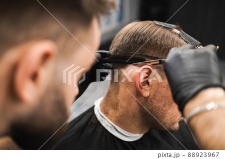 Hairdresser scissors hair on the head sides for a stylish black-haired man in the barbershop Hairdresser scissors hair on the head sides for a stylish black-haired man in the barbershop 88923967
