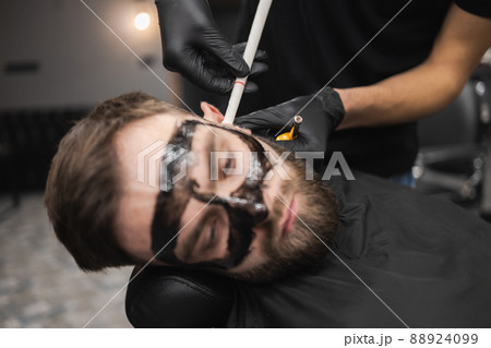 Man in a beauty salon is removing earwax using candles. 88924099