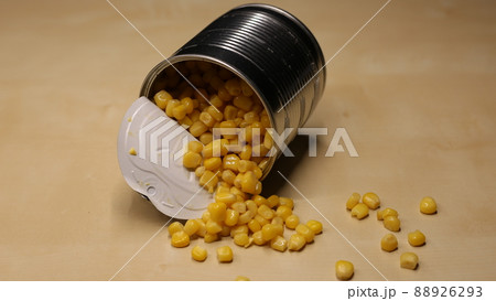 Yellow corn is scattered on the table. A can of canned corn with juice is open and stands on a wooden table 88926293