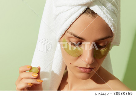 Woman using grapeseed-based eye patches on pastel green background. Natural sustainable skincare 88930369