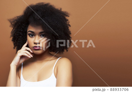 pretty young african american woman with curly hair posing cheerful gesturing on brown background, lifestyle people concept 88933706