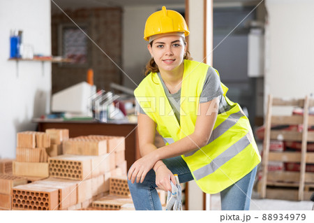 Confident female builder in yellow vest and hard hat at construction site 88934979