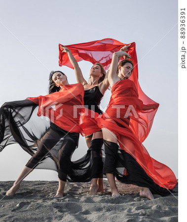 Three girls in black and red flowing fabric pose on sand dune Three girls in black and red flowing fabric pose on sand dune 88936391