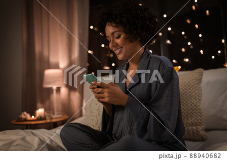 happy woman in pajamas with phone in bed at night 88940682