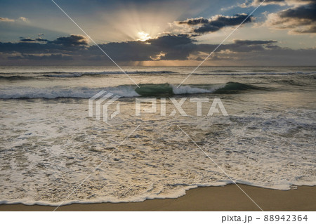 Rising sun shining through clouds above ocean 88942364
