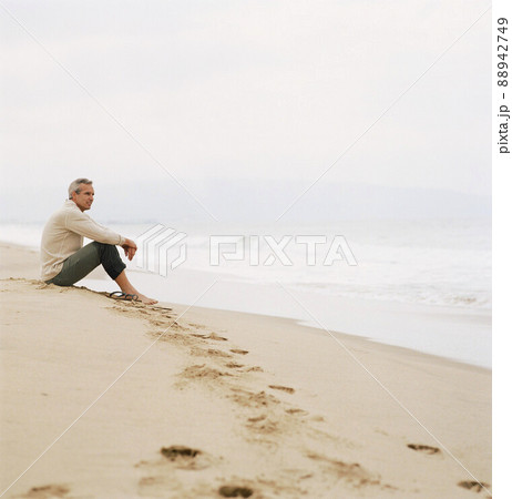 Man sitting on beach looking at ocean Man sitting on beach looking at ocean 88942749
