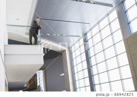 Businessman leaning on balcony in building lobby Businessman leaning on balcony in building lobby 88942825
