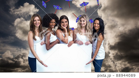 Group of diverse young women holding a blank placard with copy space against clouds in the sky 88944089