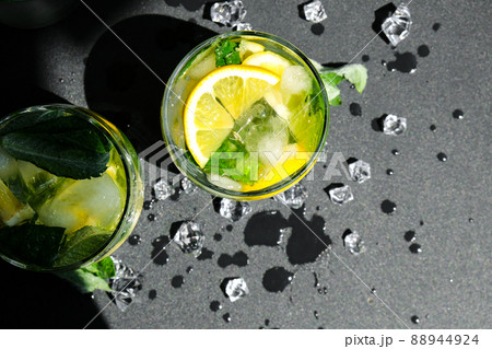 Mojito refreshing cocktail, alcohol drink. Lemonade with lemon and mint leaves on dark background. Ice cubes. Summer refreshing detox drinks. Clean eating, healthy lifestyle concept. Top view Mojito refreshing cocktail, alcohol drink. Lemonade with lemon and mint leaves on dark background. Ice cubes. Summer refreshing detox drinks. Clean eating, healthy lifestyle concept. Top view 88944924
