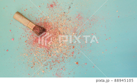 Top view of a small blush applicator brush, with a pile of pinkish makeup powder center around the brush head. On a bluish green background. With copy space on the right. Top view of a small blush applicator brush, with a pile of pinkish makeup powder center around the brush head. On a bluish green background. With copy space on the right. 88945105