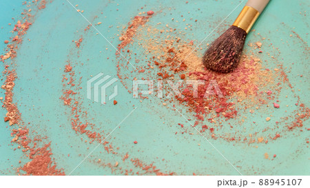 A large blush applicator brush, with a pile of red and cream color makeup powder center around the brush head. On a bluish green background. A large blush applicator brush, with a pile of red and cream color makeup powder center around the brush head. On a bluish green background. 88945107