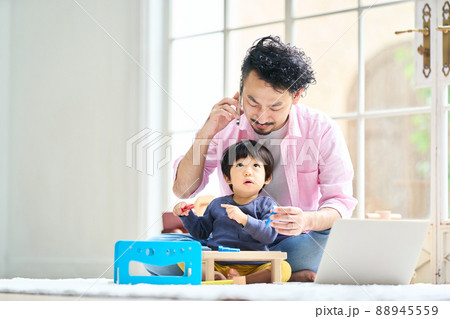 1歳10ヶ月の男の子の子守りをしながらテレワークする髭男性の写真素材