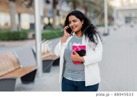 An Indian girl is walking around the city and talking on the phone. 88945633