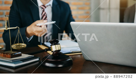Male judge in a courtroom the gavel, working with digital tablet computer on wood table in sun light. Male judge in a courtroom the gavel, working with digital tablet computer on wood table in sun light. 88947202