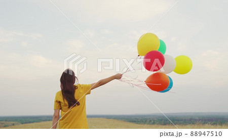 young girl with air beautiful balloons against blue sky. walk child nature. festive mood teenager. happy carefree. hold gel balls hand. blue green red orange yellow colors. fun one person journey. 88947510