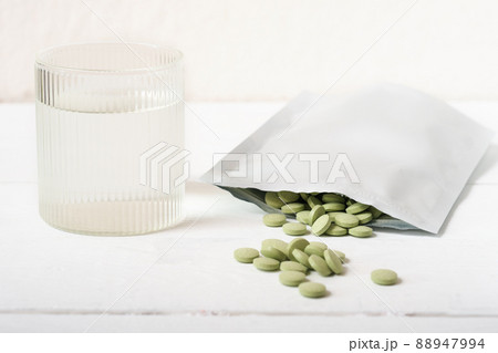 barley grass pills on a table next to glass of water. Spirulina and chlorella tablets for detox and metabolism supplement. raw vegan superfood. 88947994