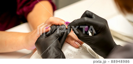 Professional manicure. A manicurist is painting the female nails of a client with purple nail polish in a beauty salon, close up. Beauty industry concept Professional manicure. A manicurist is painting the female nails of a client with purple nail polish in a beauty salon, close up. Beauty industry concept 88948986