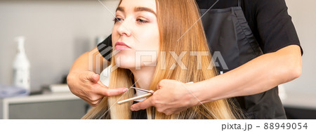 Beautiful young blonde woman with long straight blonde hair getting a haircut at the hairdresser salon 88949054