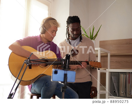 A personal afroamerican tutor explains to his asian student how to play studied chord correctly. Musical education at home A personal afroamerican tutor explains to his asian student how to play studied chord correctly. Musical education at home 88950275