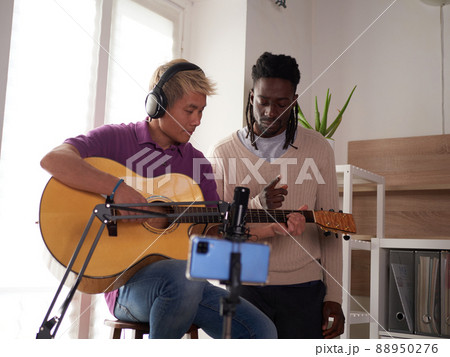 A personal afroamerican tutor explains to his asian student how to play studied chord correctly. Musical education at home A personal afroamerican tutor explains to his asian student how to play studied chord correctly. Musical education at home 88950276
