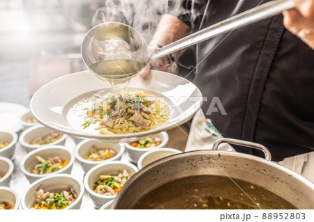 Chef pours broth into a chicken soup with noodles, meat and vegetable 88952803