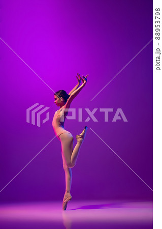 Portrait of young little ballet dancer, teen practicing, dancing isolated on purple background in neon light. Art, grace, beauty, ballet school concept 88953798